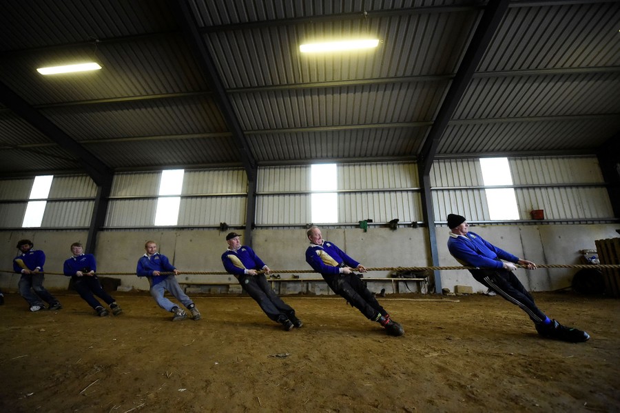 Several men lean while pulling on a thick rope inside a building.