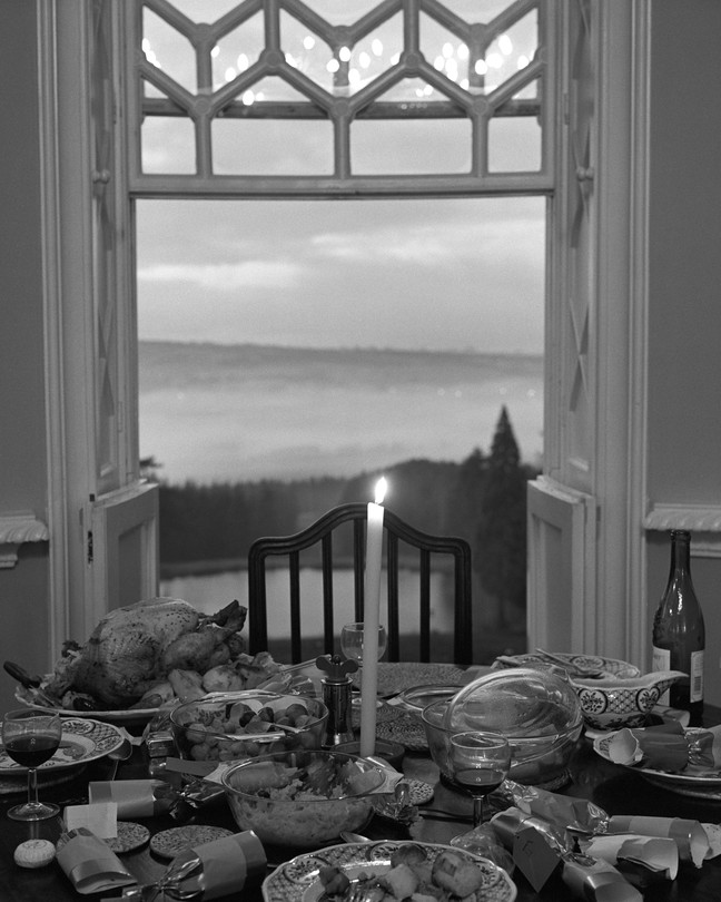 A table set with food and wine and a lit candle, with a door open in the background showing the sky
