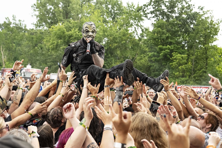 A performer wearing a mask crowd-surfs during an outdoor concert.