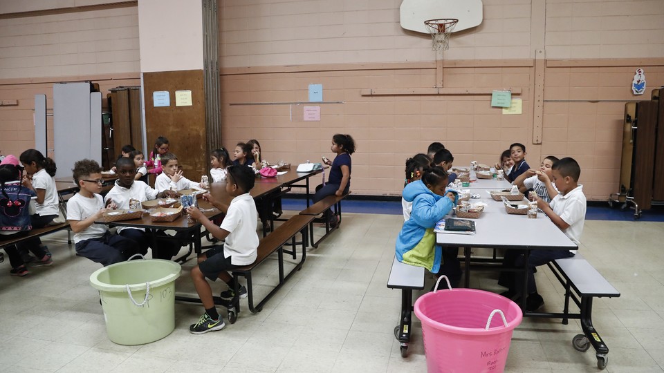 A group of children eats at two long lunch tables.