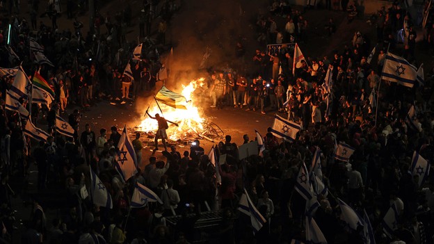 Picture that shows protesters blocking a road and holding national flags as they gather around a bonfire during a rally against the Israeli government's judicial reform in Tel Aviv, Israel on March 27, 2023.