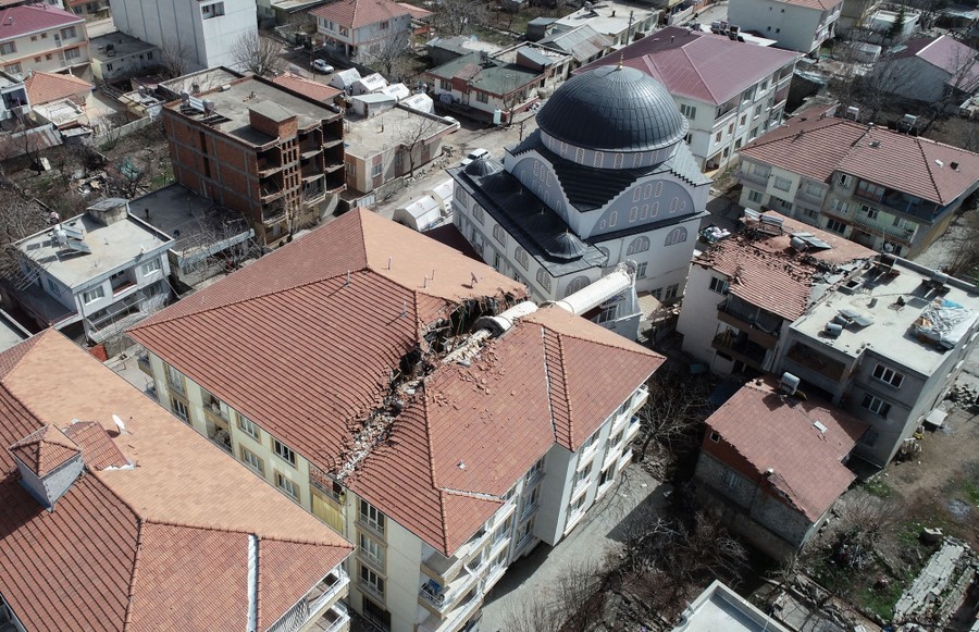 An aerial view of a damaged three-story building after a nearby minaret fell across it