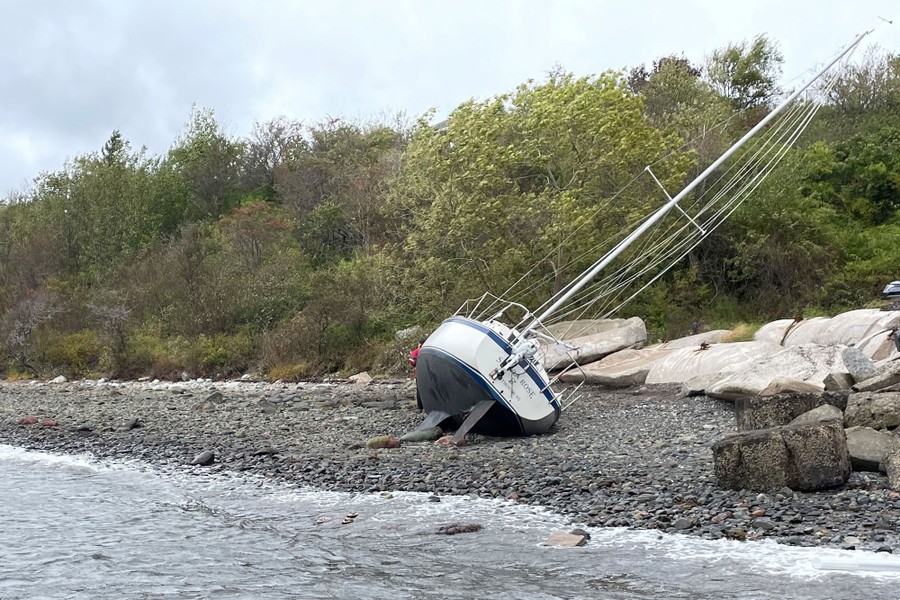 A sailboat lies on its side, washed up on shore.