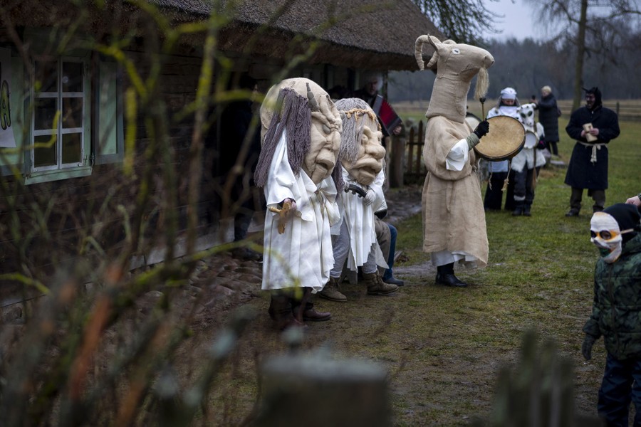 Several people in traditional costumes perform outside a house.