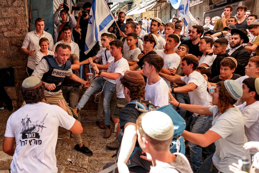 A crowd of mostly young Israeli men rushes toward a Palestinian man wearing a vest that says "Press" on it.
