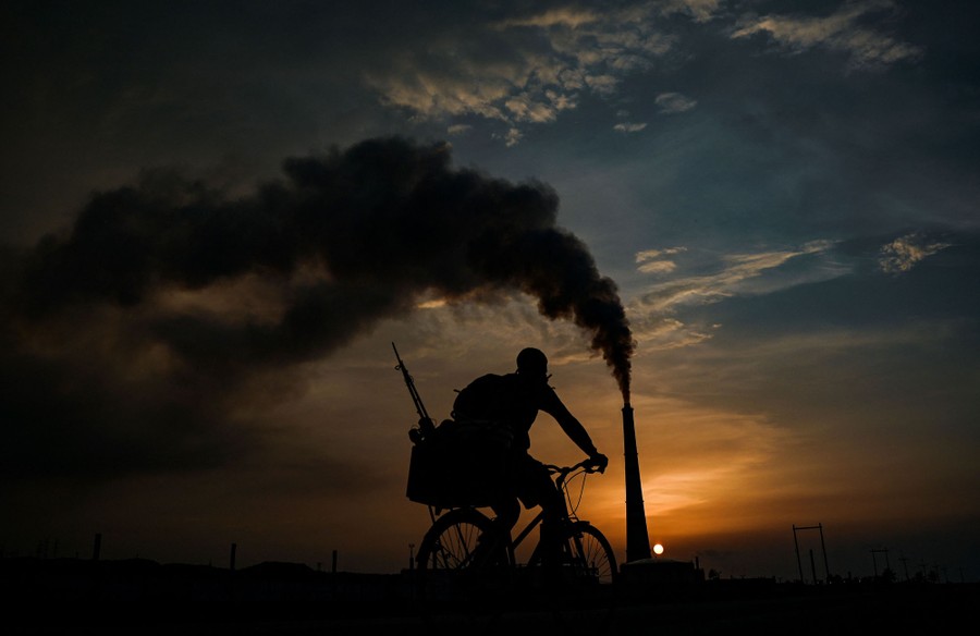 A man rides his bike past a power plant.