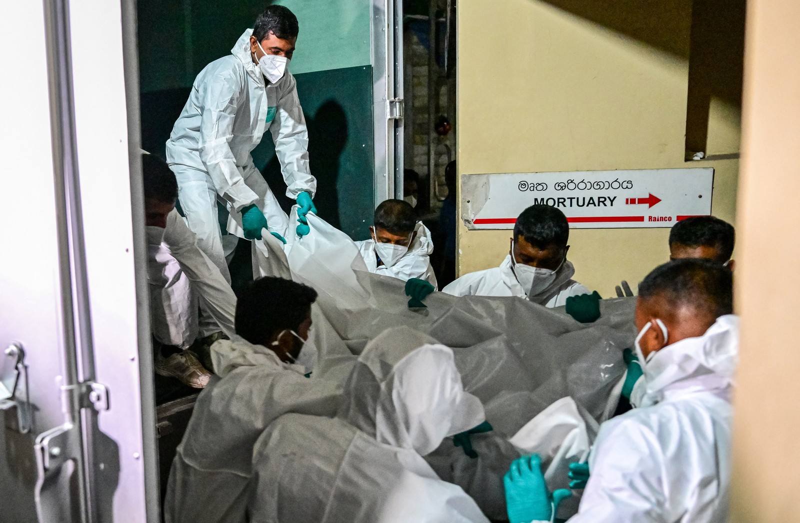 Workers wearing protective suits carry bagged bodies from a truck into a mortuary.