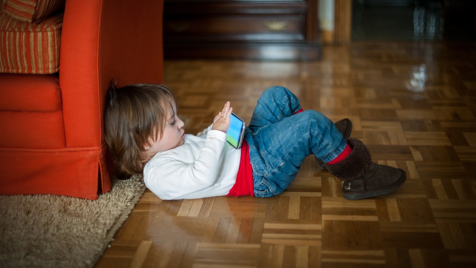A child on the floor looking at a smartphone