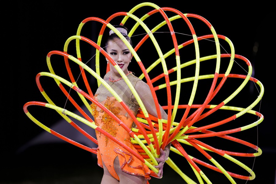 A circus performer poses with numerous hoops fanned out over and around their body.