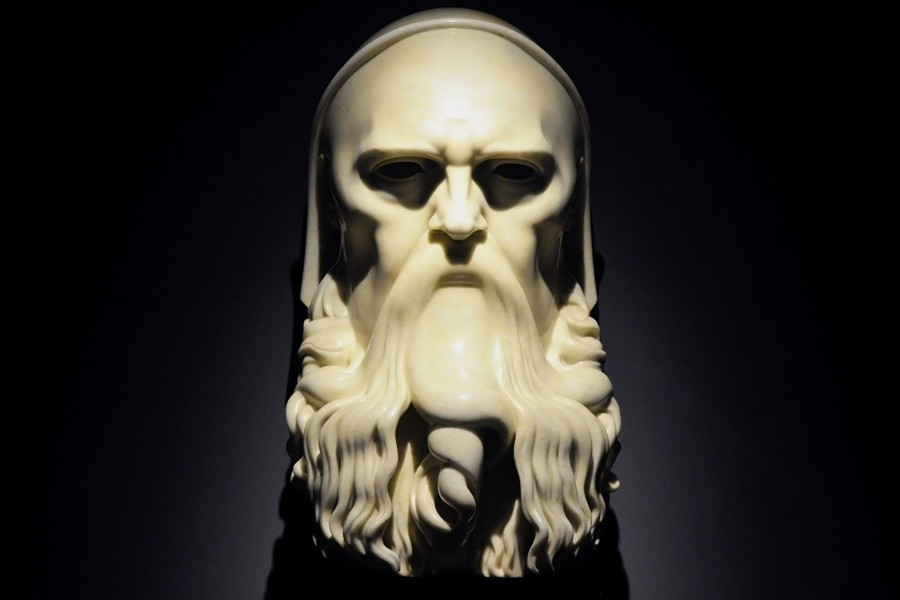 A starkly-lit marble sculpture of a bearded man's head