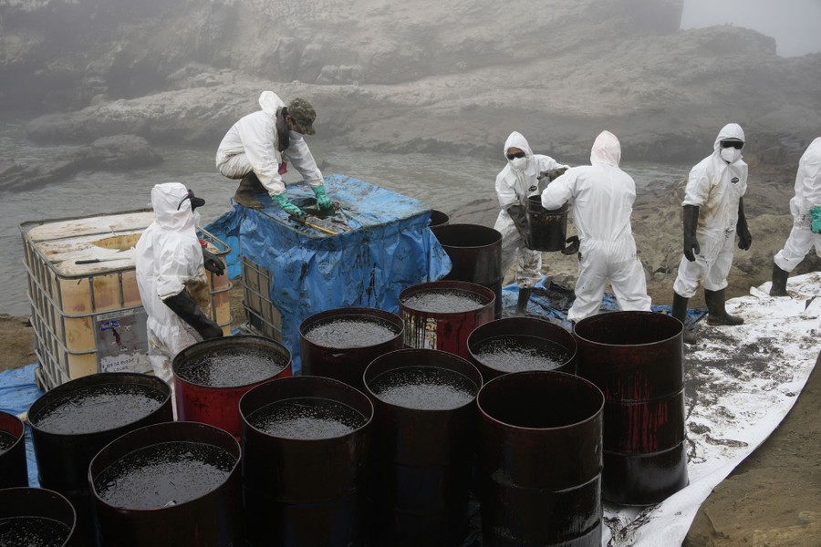 A half-dozen workers transport spilled oil by bucket into waiting barrels.