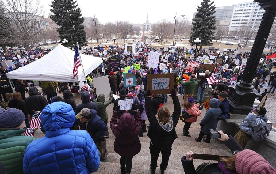 A crowd of protesters gathers on the steps of a state capitol building.