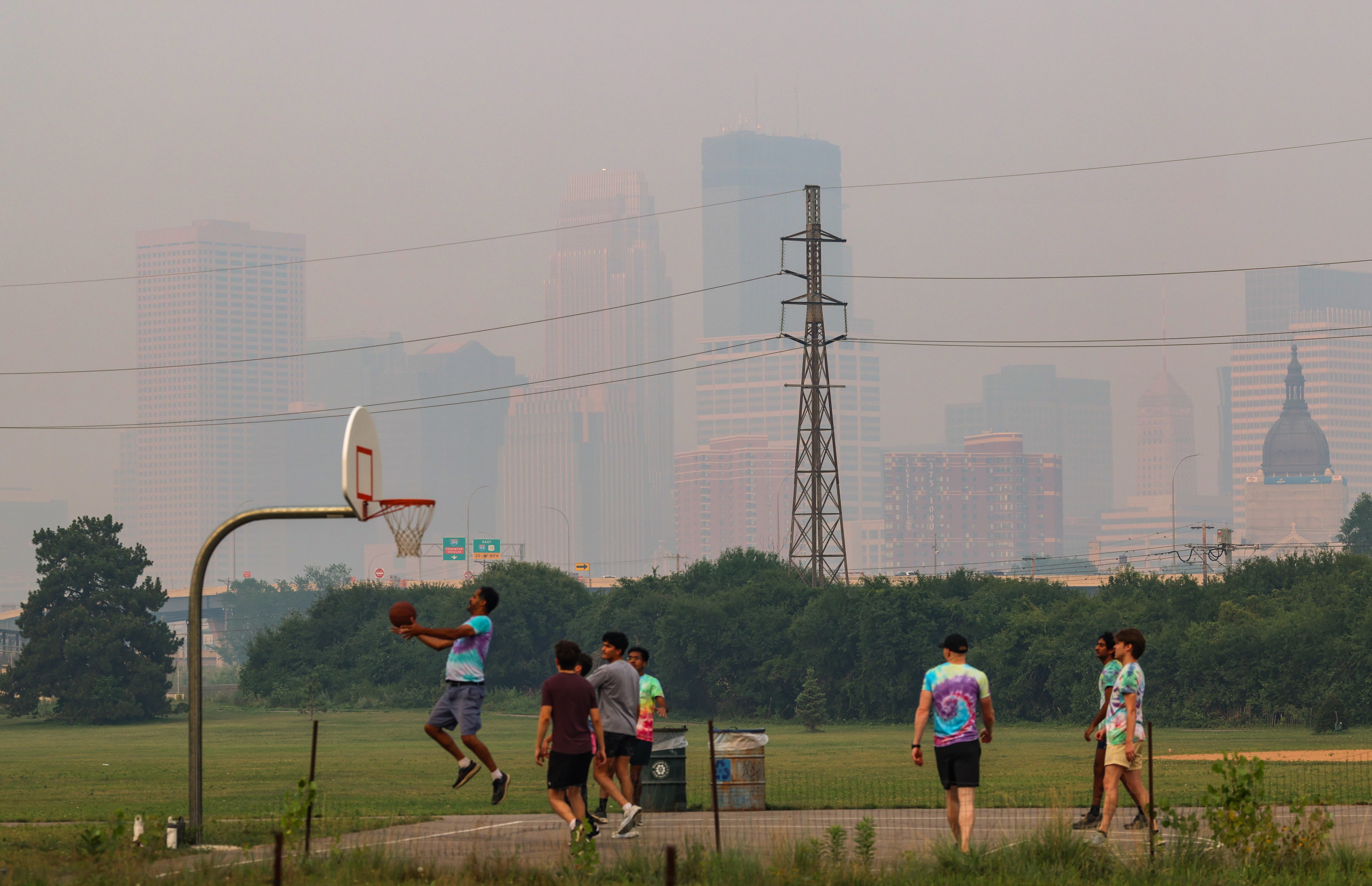 People play basketball as the Minneapolis skyline is obscured by wildfire smoke in the background.