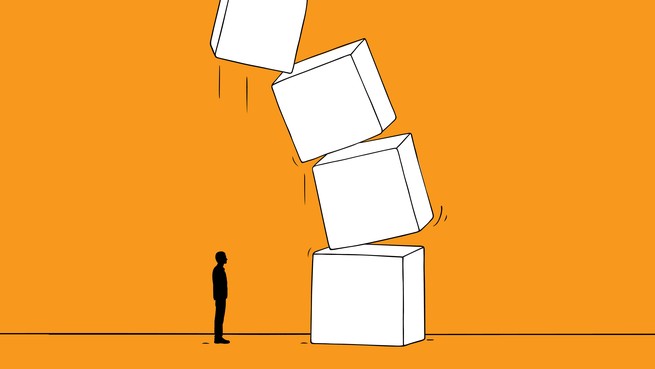 A small figure stands in front of a big stack of toppling boxes