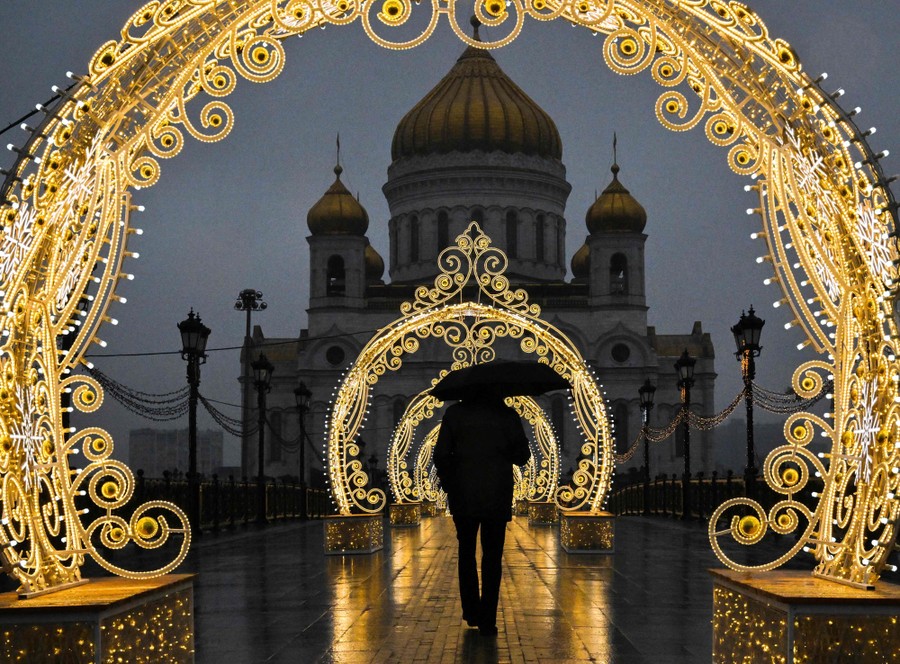 A person walks beneath illuminated arches in front of a cathedral.