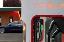 A Tesla Supercharger in the foreground, with a car in the background