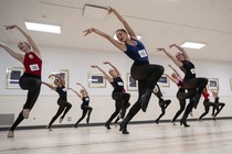 About a dozen dancers perform together in a studio during an audition.