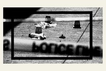 Black-and-white photo of police tape across a crime scene with numbered evidence markers