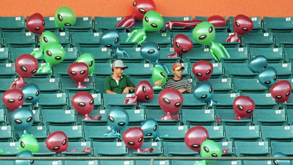 Two boys sit in a stadium surrounded by inflatable aliens
