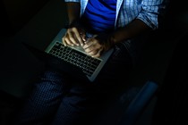 A person typing on a laptop in the dark