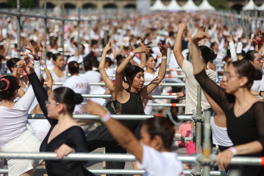 Hundreds of people practice ballet moves together outside, in a city square.