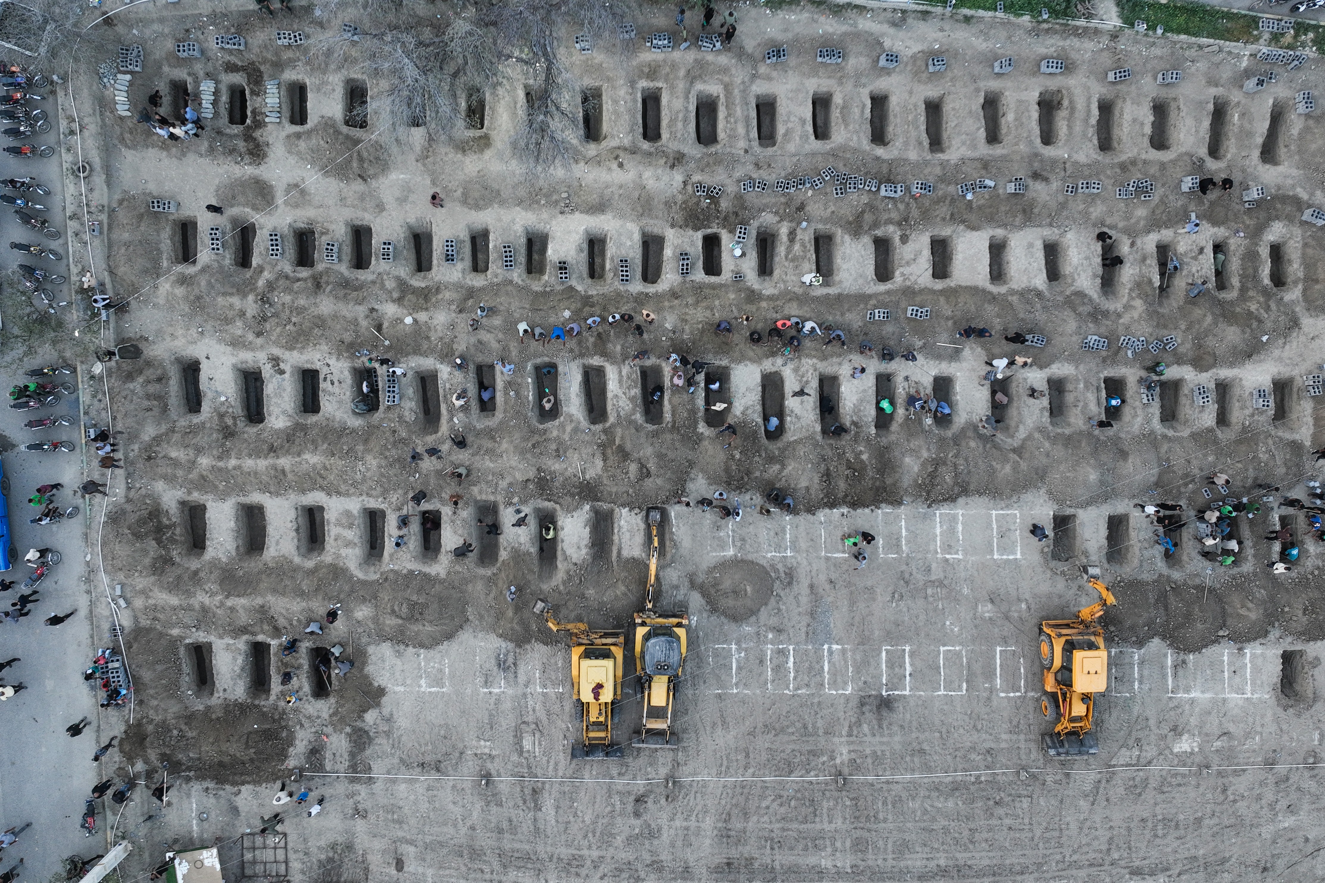 An aerial view of about 100 graves being dug, in several rows.