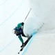 A freestyle skier grinds along the lip of an Olympic halfpipe, kicking up snow.