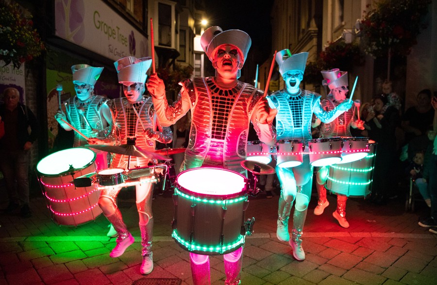 Costumed and brightly lit drummers march in a festival parade.