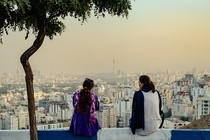 Two women with uncovered hair sit on a wall overlooking the city of Tehran.