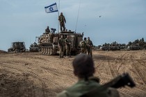 In the desert near the Israel-Gaza border, a tank with soldiers atop and alongside flies the Israeli flag.