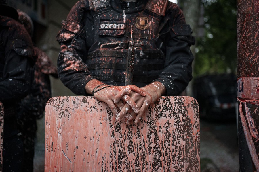A police officer holds a shield; both he and it are covered in paint splatters.