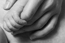 Black-and-white photograph of an adult hand holding a newborn's leg