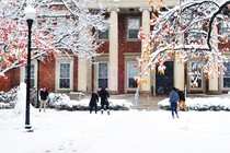 Students have a snowball fight in front of a large brick building with columns.