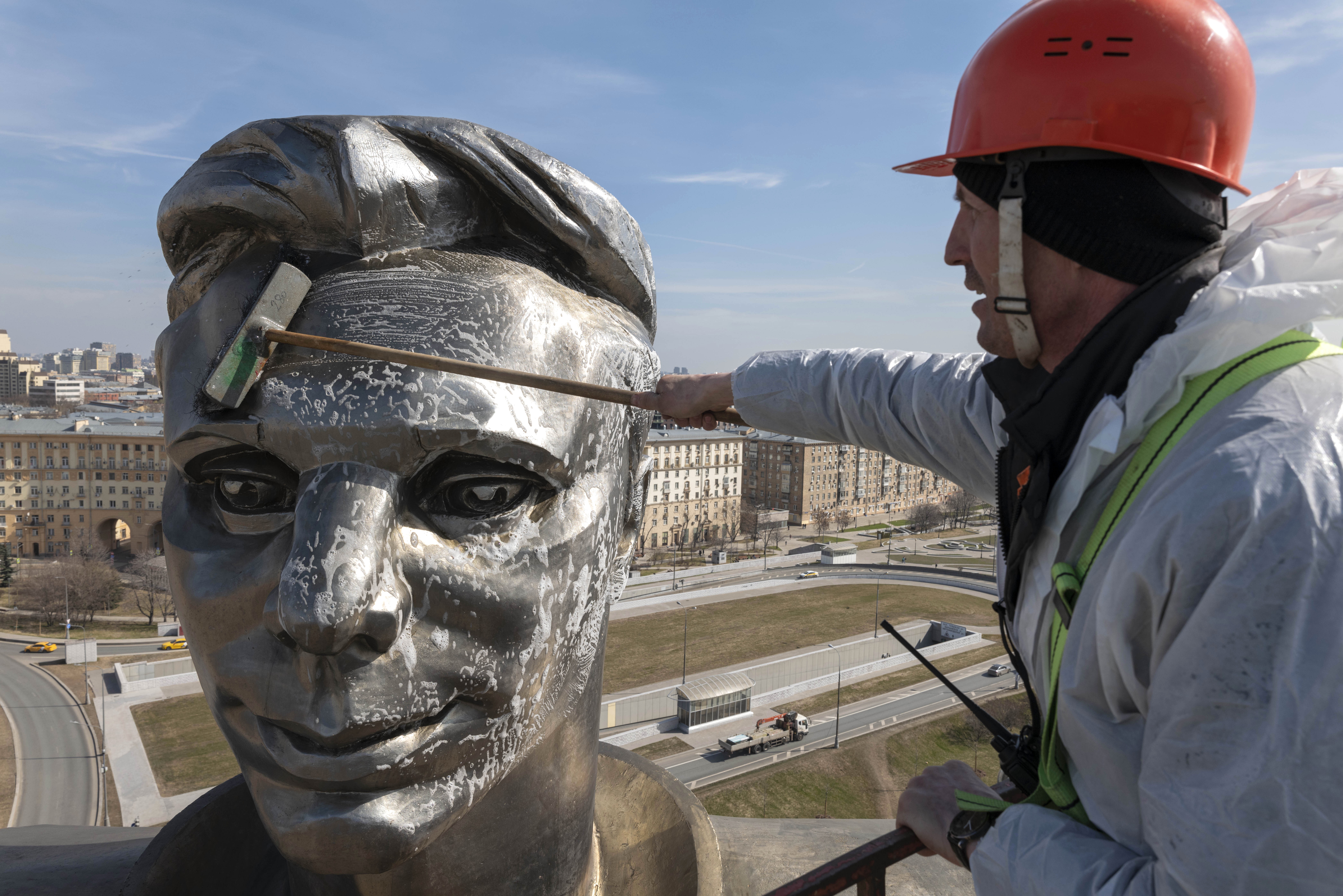 A cleaner uses a brush on the soap-covered face of a large statue.