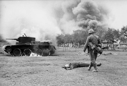 German infantryman walks by a fallen Soviet soldier and a burning Soviet tank