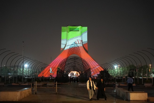 People walk in front of an illuminated monument at the Azadi Square