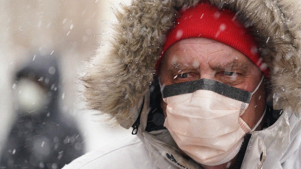 A man wearing a face mask walks through the snow.