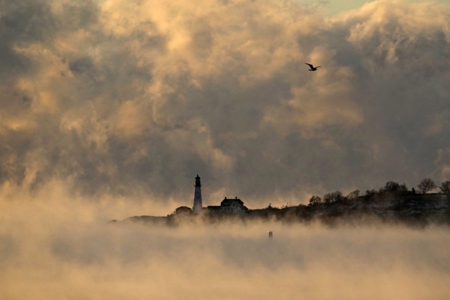 A lighthouse is visible beyond a harbor with steam rising off it.