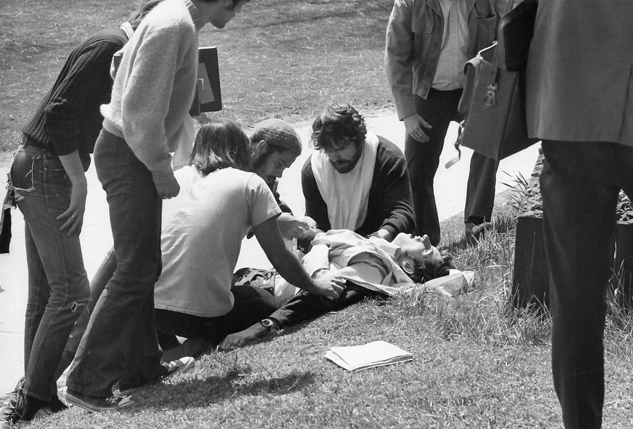 Several people tend to an injured person lying on their back beside a pathway.