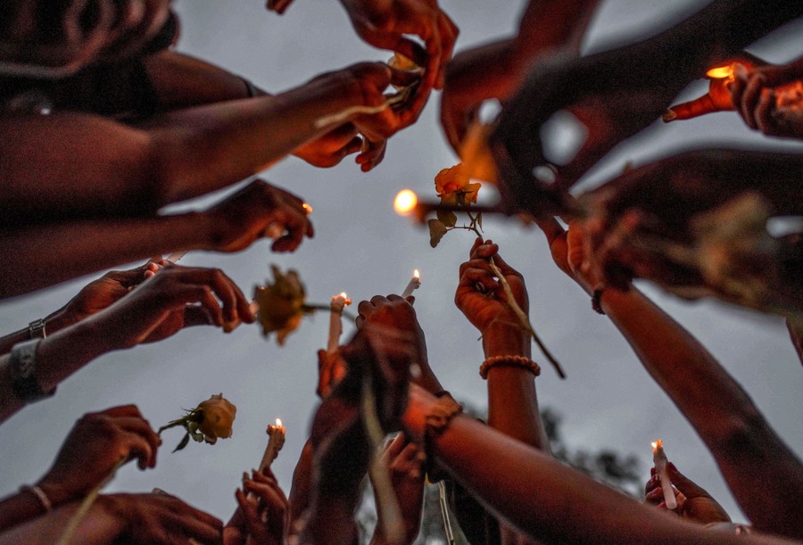 People hold up candles and flowers during a memorial.