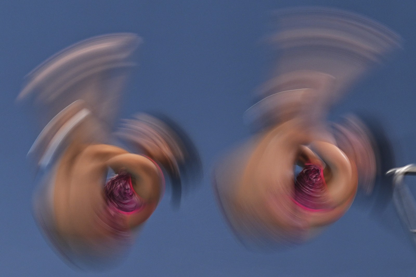 A pair of synchronized divers, seen mid-jump, their arms and legs blurred by their spinning motion