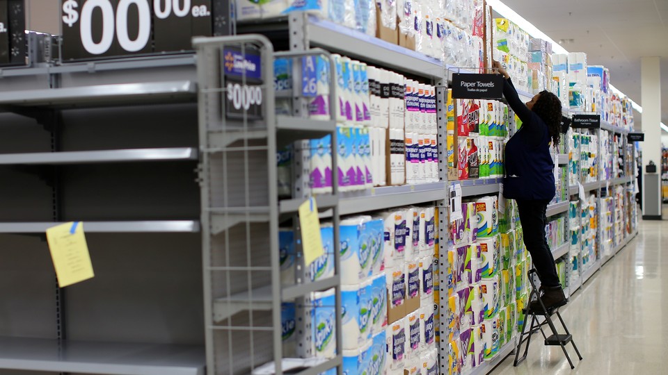 A Walmart employee stocks rolls of paper towels on a shelf.