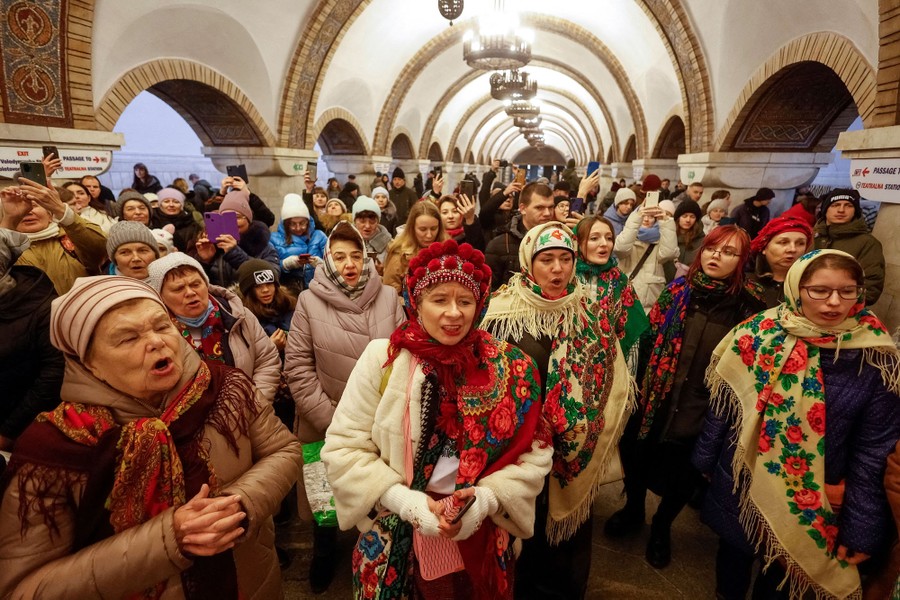 A crowd of people inside a metro station sing together.