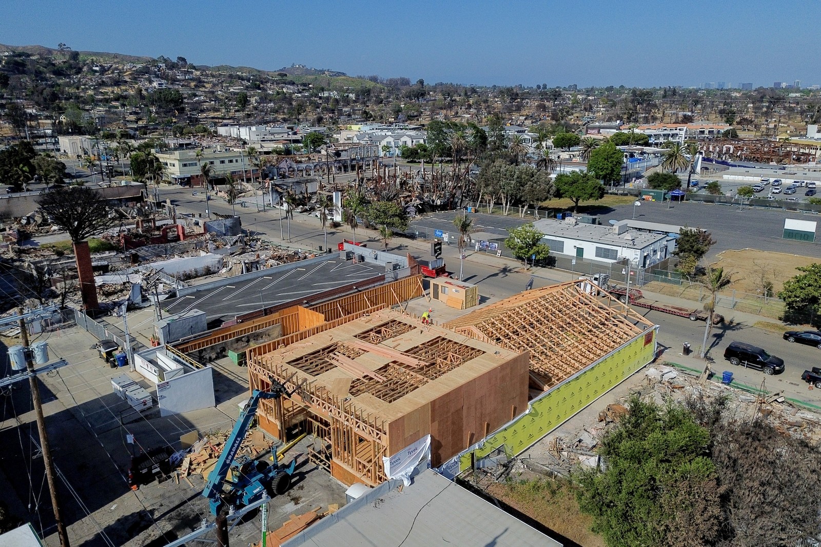 An aerial view of a fire-damaged neighborhood, with a large building under construction in the foreground.