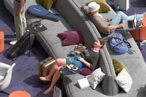 detail from illustration of travelers relaxing on large gray sofa in purple-carpeted lounge