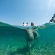 A girl rides a horse in the water, seen both above and under the water.