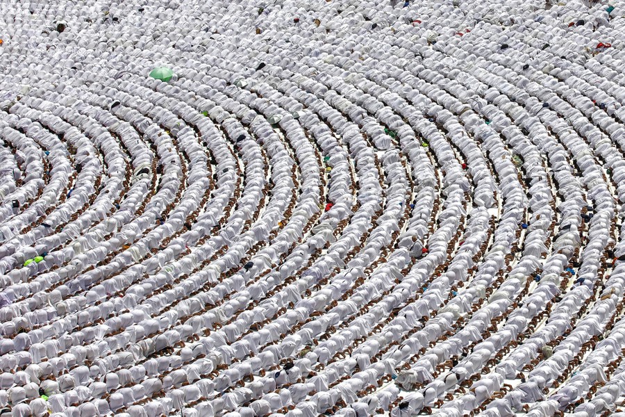 Hundreds of worshippers gathered in concentric rows and dressed in white kneel down in prayer.