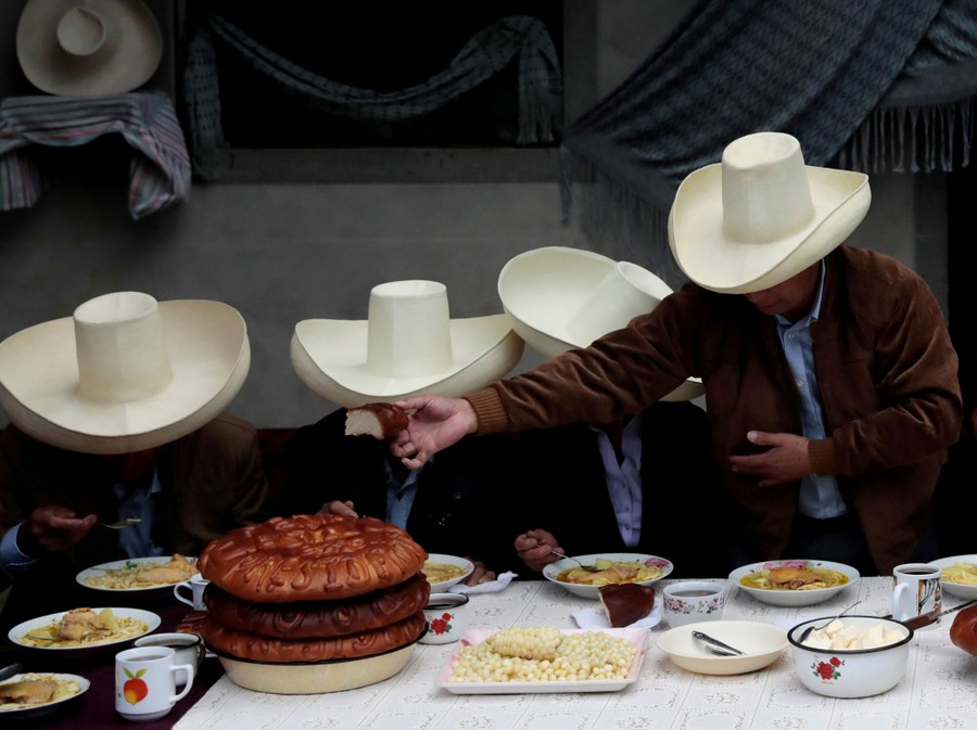 Four people wearing large hats share bread at breakfast.