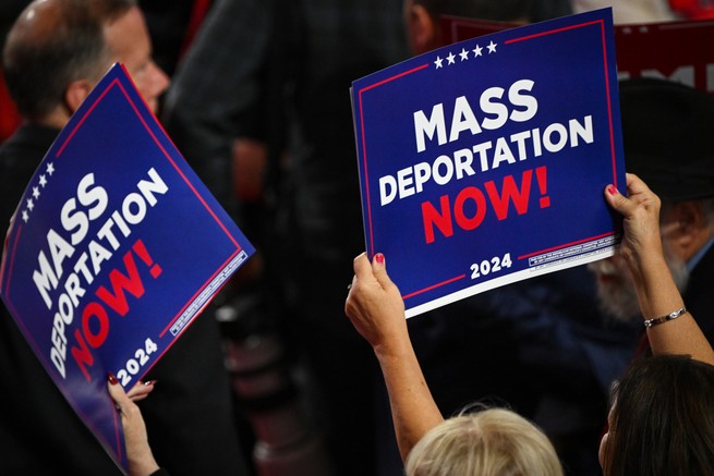 People hold up signs at a Trump rally that say "Mass Deportation Now 2024"