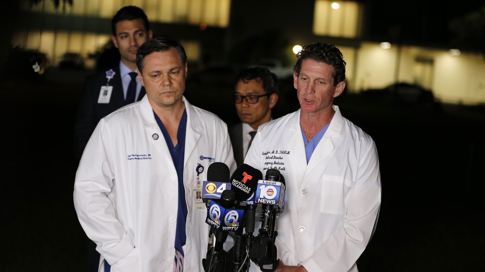 Two doctors in white coats stand in front of microphones